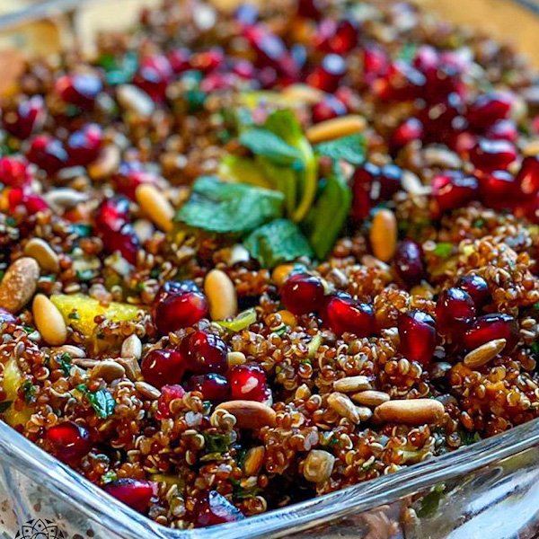 Red quinoa salad with roasted sweet potato, avocado, pine nuts and pomegranate seeds in a white bowl